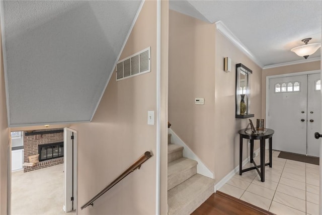 tiled entryway featuring visible vents, stairs, a textured ceiling, crown molding, and a brick fireplace