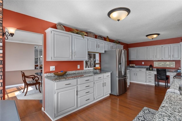 kitchen with white cabinetry, light stone counters, dark wood-type flooring, and stainless steel fridge with ice dispenser