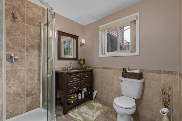 bathroom with toilet, a wainscoted wall, vanity, tile walls, and a stall shower