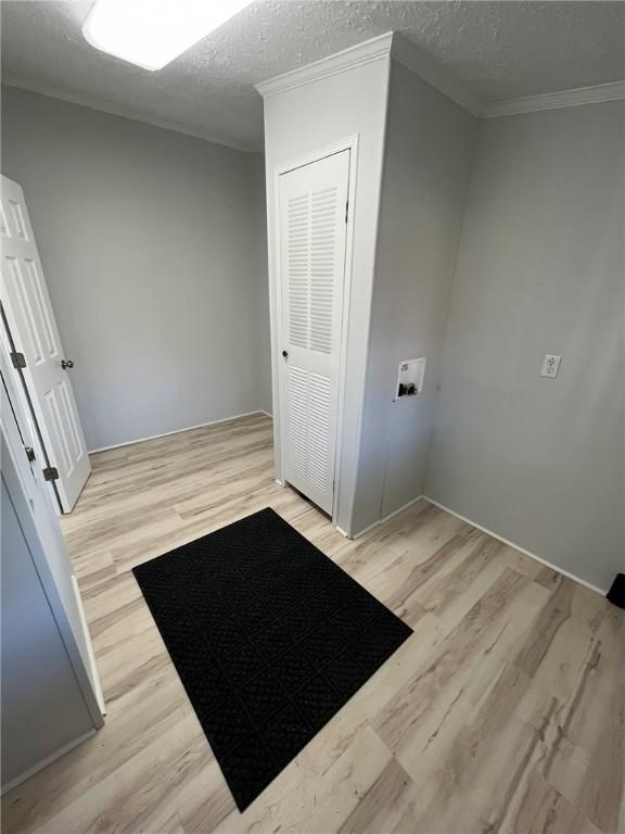 clothes washing area with laundry area, a textured ceiling, crown molding, and wood finished floors
