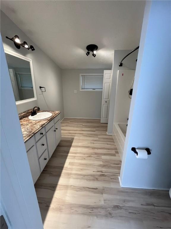 bathroom featuring baseboards, washtub / shower combination, wood finished floors, and vanity
