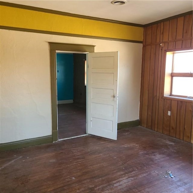 empty room with baseboards, wooden walls, dark wood-style floors, and ornamental molding