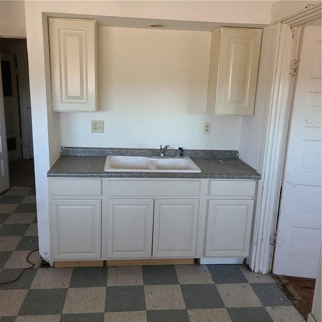 kitchen with a sink, light floors, dark countertops, and white cabinets