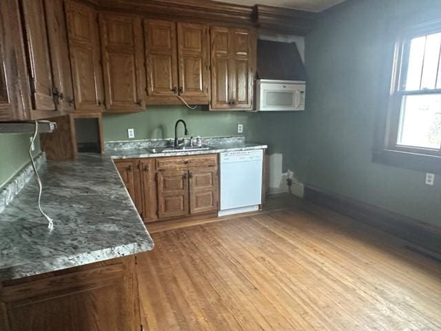 kitchen featuring baseboards, light wood-type flooring, white appliances, brown cabinets, and a sink