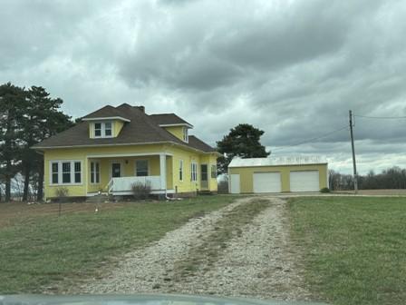 view of front of house featuring covered porch, a garage, an outbuilding, a front lawn, and driveway