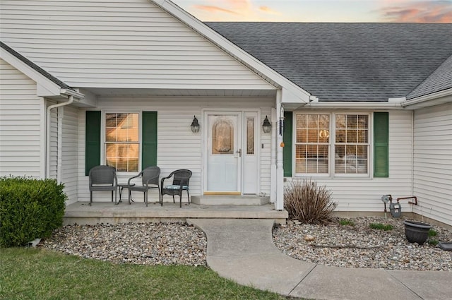 exterior entry at dusk with a porch and a shingled roof