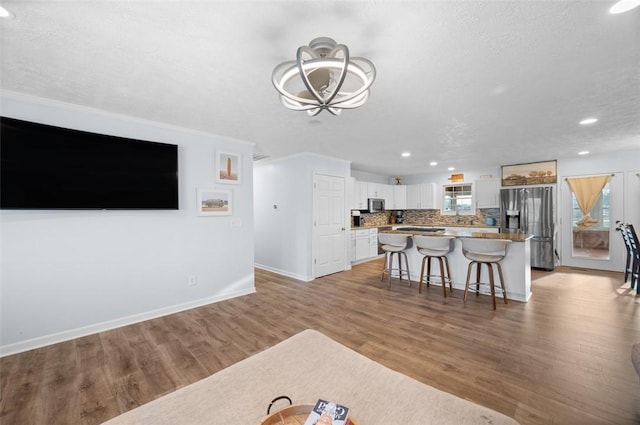 living area featuring a textured ceiling, baseboards, recessed lighting, light wood-style floors, and a notable chandelier