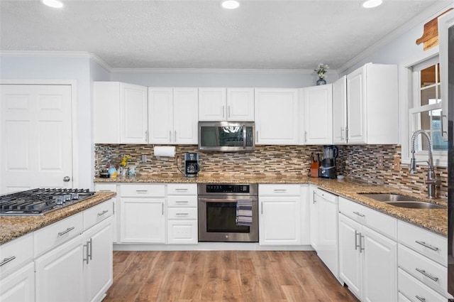 kitchen featuring crown molding, stainless steel appliances, white cabinetry, a sink, and light wood-type flooring