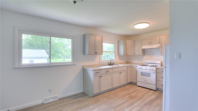 1302 Clement Ave, Forsyth, IL 62535 - kitchen with white gas range oven, a sink, under cabinet range hood, light countertops, and light wood-style floors