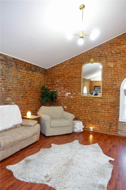 unfurnished living room featuring hardwood / wood-style floors, lofted ceiling, and brick wall