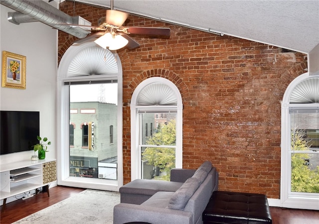 living room with ceiling fan, dark wood-type flooring, brick wall, a textured ceiling, and lofted ceiling