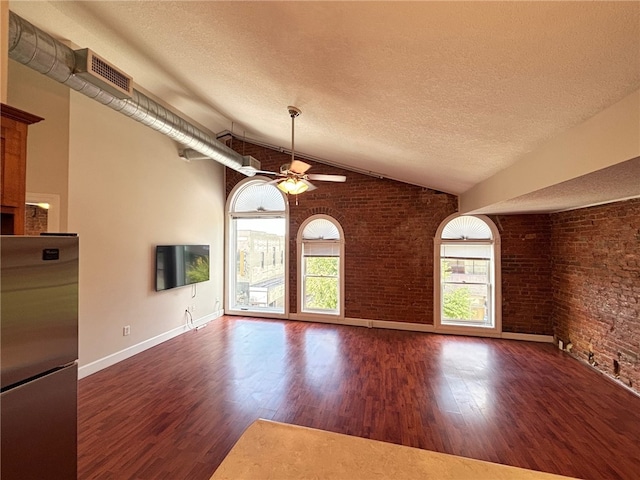 unfurnished living room featuring ceiling fan, dark wood-type flooring, brick wall, a textured ceiling, and lofted ceiling