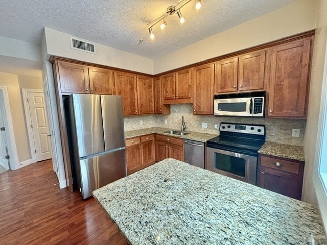 kitchen with light stone countertops, sink, stainless steel appliances, dark hardwood / wood-style flooring, and a textured ceiling