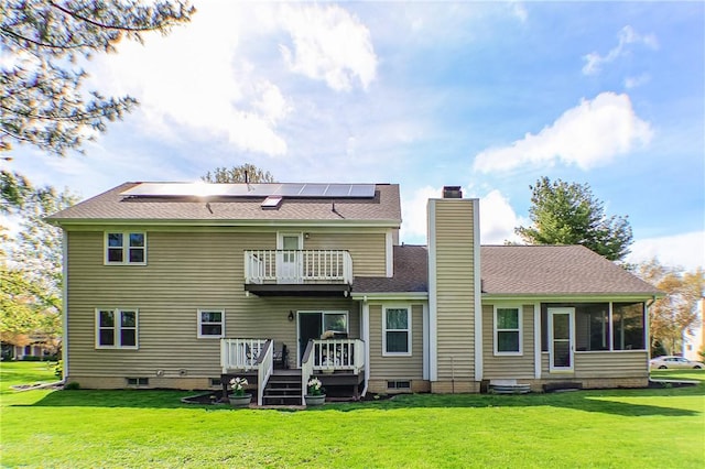 back of house featuring a chimney, a deck, roof mounted solar panels, a balcony, and a yard