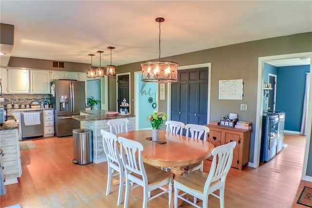 dining space featuring an inviting chandelier, light wood finished floors, independent washer and dryer, and visible vents