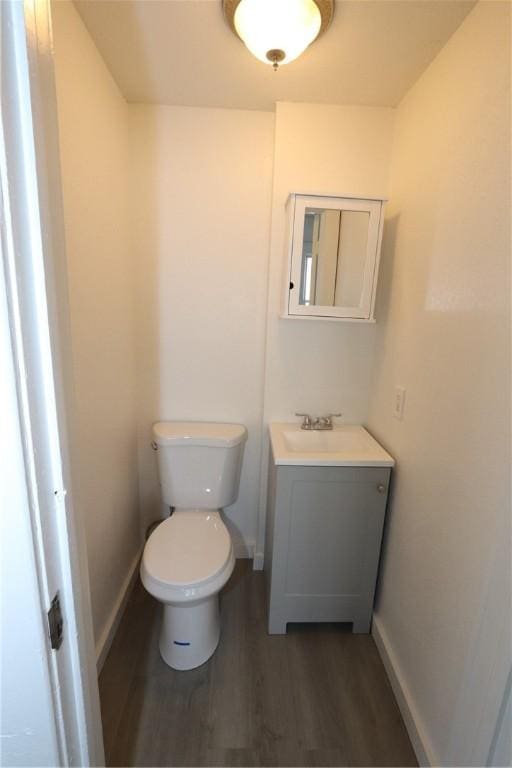 half bathroom with baseboards, toilet, wood finished floors, and vanity