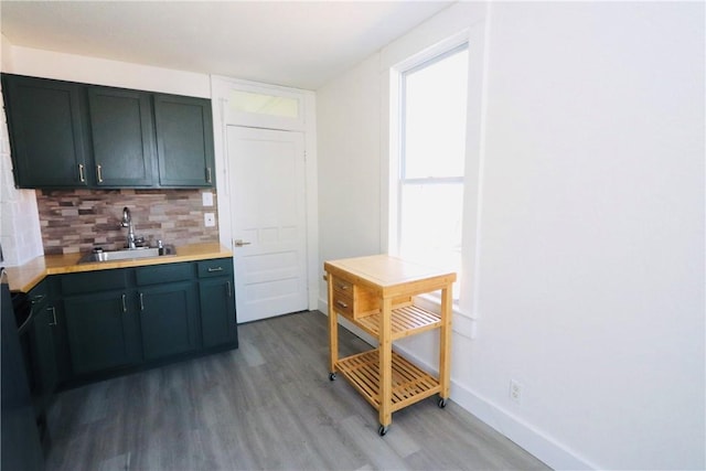 kitchen featuring light wood-type flooring, a sink, tasteful backsplash, light countertops, and baseboards