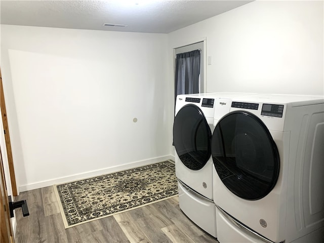 washroom with light hardwood / wood-style flooring, washing machine and dryer, and a textured ceiling