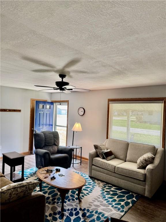 living area featuring baseboards, a textured ceiling, ceiling fan, and wood finished floors