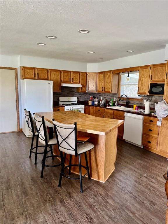 kitchen featuring white appliances, dark wood-style floors, under cabinet range hood, and a sink