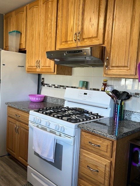 kitchen featuring dark stone countertops, white appliances, dark wood-type flooring, and decorative backsplash