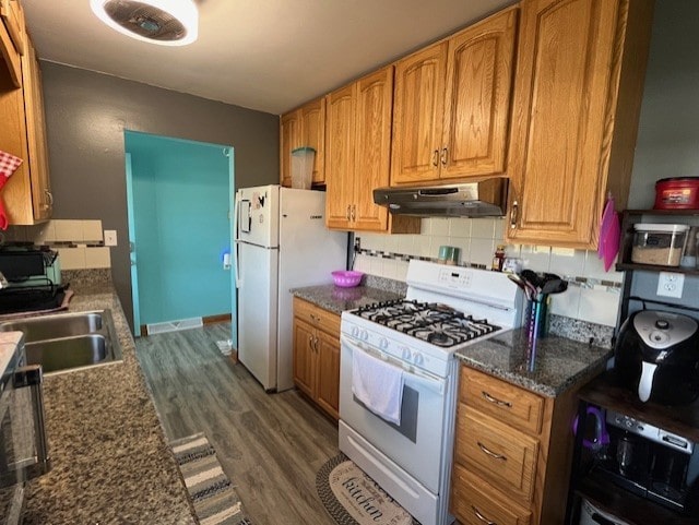 kitchen with sink, dark hardwood / wood-style flooring, dark stone counters, decorative backsplash, and white appliances