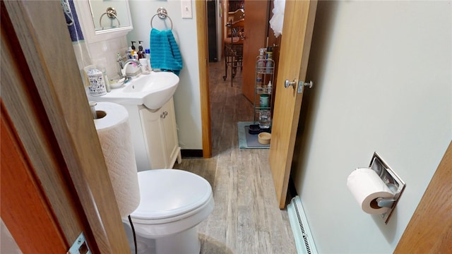 half bath with a baseboard radiator, toilet, wood finished floors, and vanity