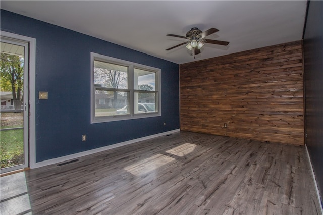 spare room featuring wood walls, plenty of natural light, ceiling fan, and hardwood / wood-style floors