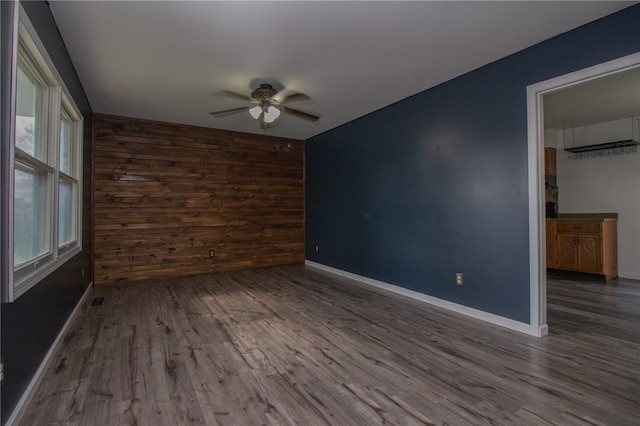 unfurnished room with wood walls, plenty of natural light, ceiling fan, and wood-type flooring