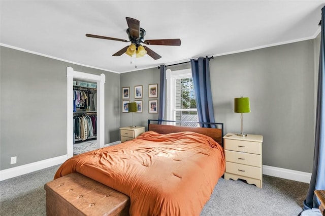 carpeted bedroom featuring a closet, ornamental molding, baseboards, a walk in closet, and ceiling fan
