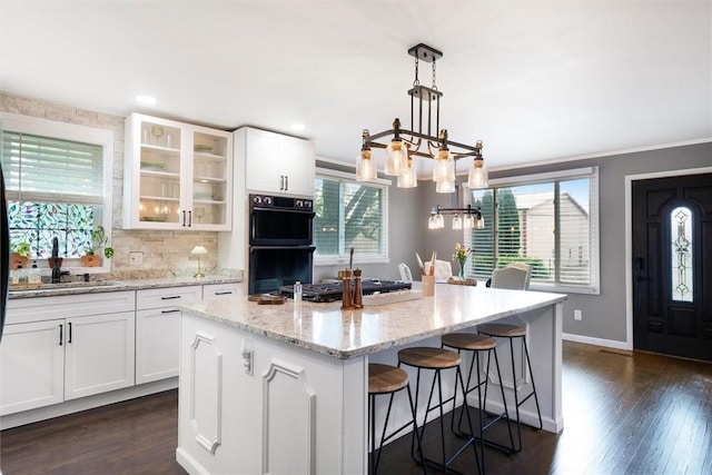 kitchen with white cabinetry, dobule oven black, plenty of natural light, and glass insert cabinets