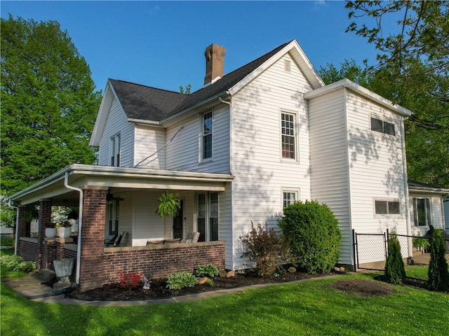 view of side of home featuring fence, brick siding, a chimney, a lawn, and covered porch