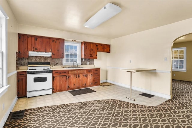 kitchen with arched walkways, white gas stove, light floors, a sink, and under cabinet range hood