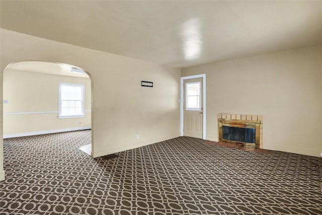 unfurnished living room with arched walkways, carpet floors, a glass covered fireplace, and baseboards