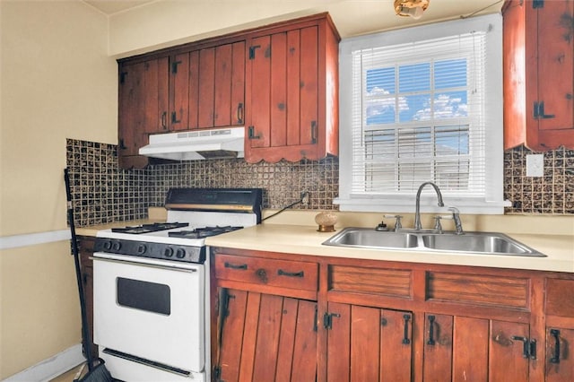 kitchen featuring white range with gas stovetop, under cabinet range hood, a sink, light countertops, and tasteful backsplash