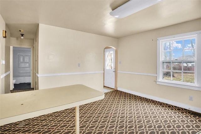 foyer with arched walkways and baseboards