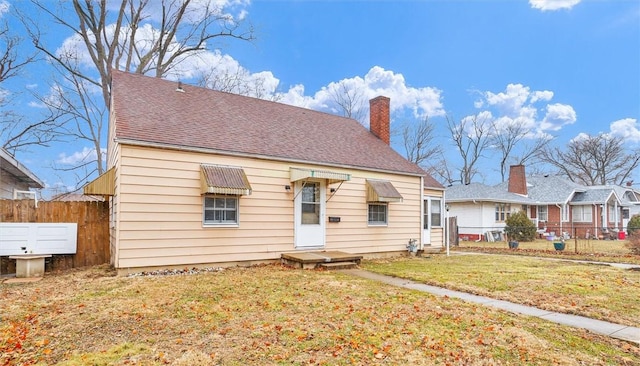 view of front of house with roof with shingles, a chimney, a front yard, and fence