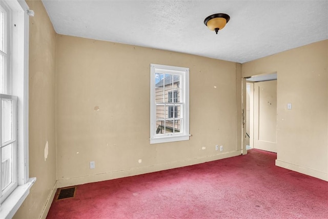 spare room with carpet floors, baseboards, visible vents, and a textured ceiling