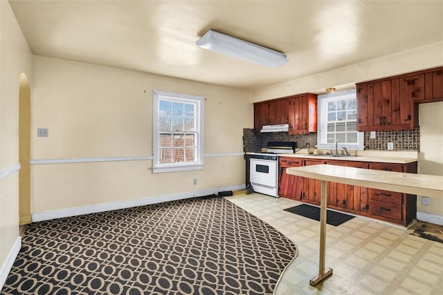 kitchen featuring under cabinet range hood, light countertops, white gas stove, light floors, and backsplash