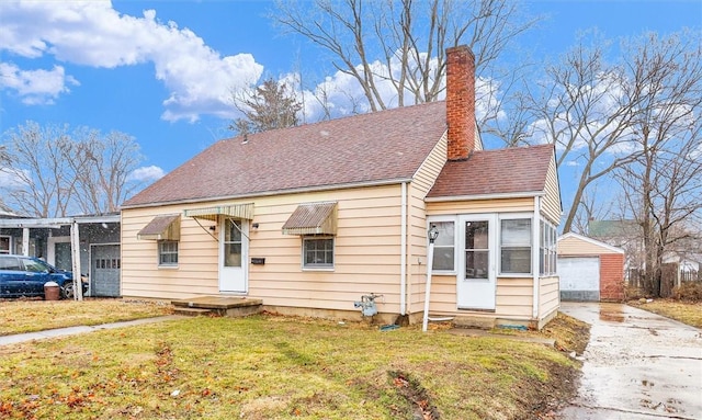 bungalow-style home featuring a garage, a chimney, roof with shingles, an outdoor structure, and a front yard