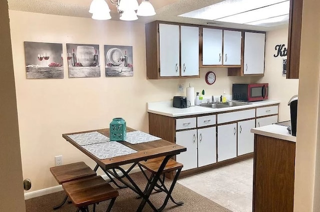 kitchen with a sink, light tile patterned flooring, pendant lighting, light countertops, and a notable chandelier