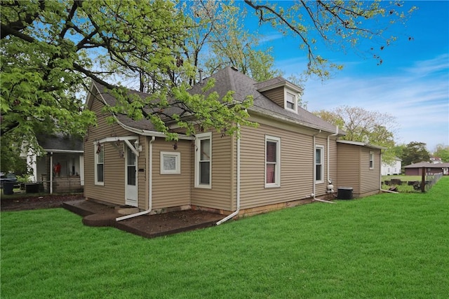 rear view of house featuring cooling unit, a shingled roof, and a yard