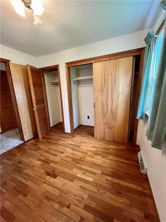unfurnished bedroom featuring two closets, light wood-style flooring, and a textured ceiling
