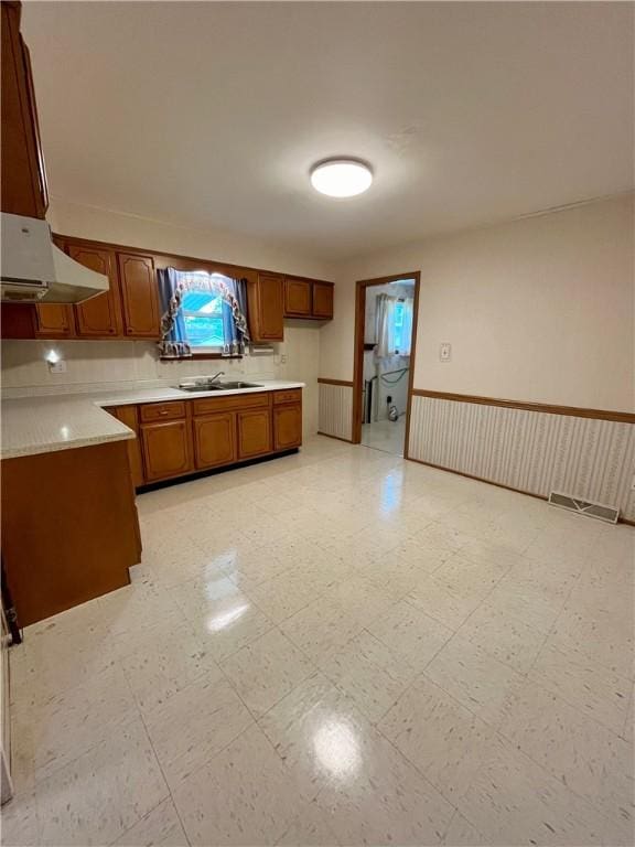 kitchen featuring brown cabinets, light countertops, a sink, and under cabinet range hood