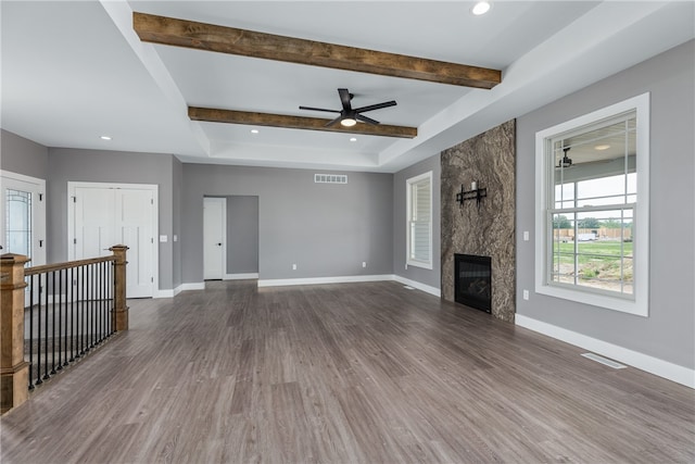 unfurnished living room with beamed ceiling, ceiling fan, dark wood-type flooring, and a premium fireplace