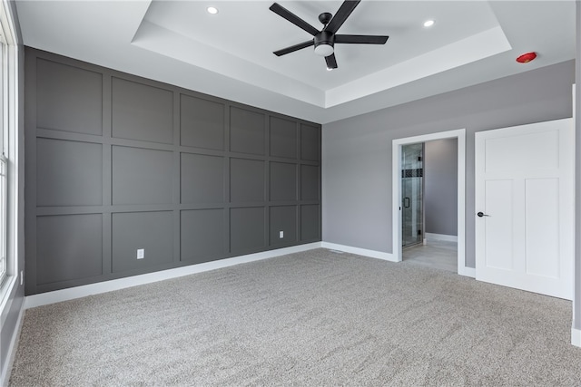 spare room with ceiling fan, a raised ceiling, and light colored carpet