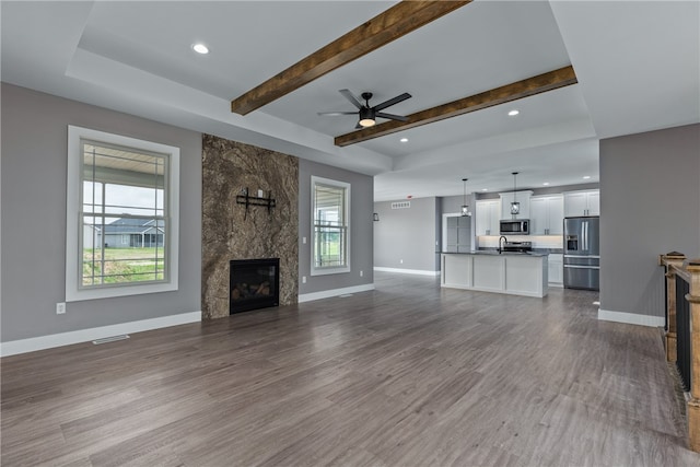 unfurnished living room with sink, hardwood / wood-style flooring, ceiling fan, a fireplace, and beamed ceiling