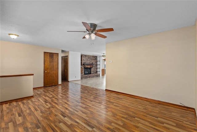 unfurnished living room featuring a brick fireplace, baseboards, ceiling fan, and wood finished floors