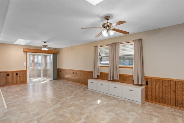 spare room featuring a skylight, a ceiling fan, a wainscoted wall, and wood walls