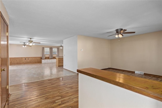 empty room featuring wood finished floors, a wainscoted wall, visible vents, ceiling fan, and a textured ceiling